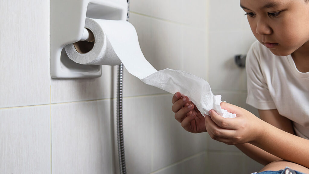 infante con diarrea sentado en el baño con papel higiénico en la mano